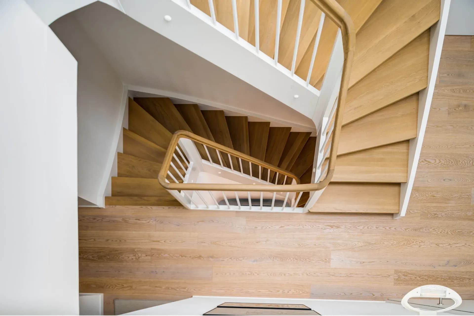 Vue du dessus d'un escalier en chêne dont les marches sont posées dans la même teinte de bois que le parquet environnant.