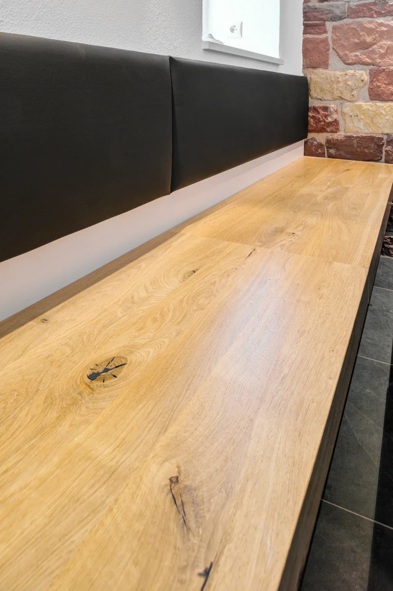 Plateau en chêne massif d'une banquette avec un veinage naturel, avec en arrière-plan une assise en cuir noir et un mur en grès.