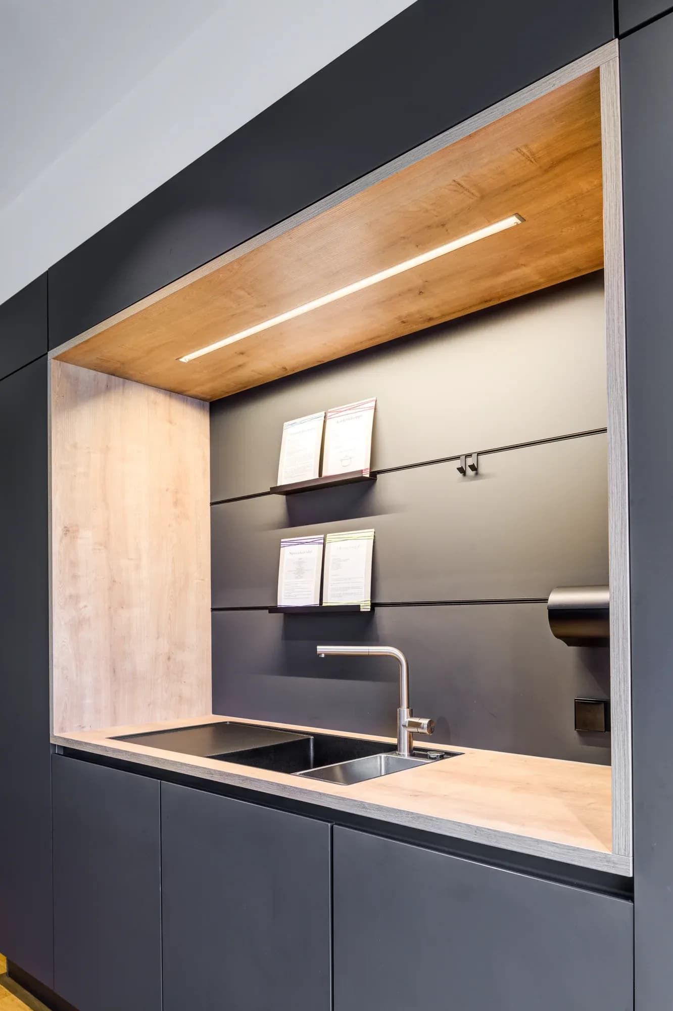 Niche éclairée en chêne dans un mur de cuisine anthracite avec évier affleurant.