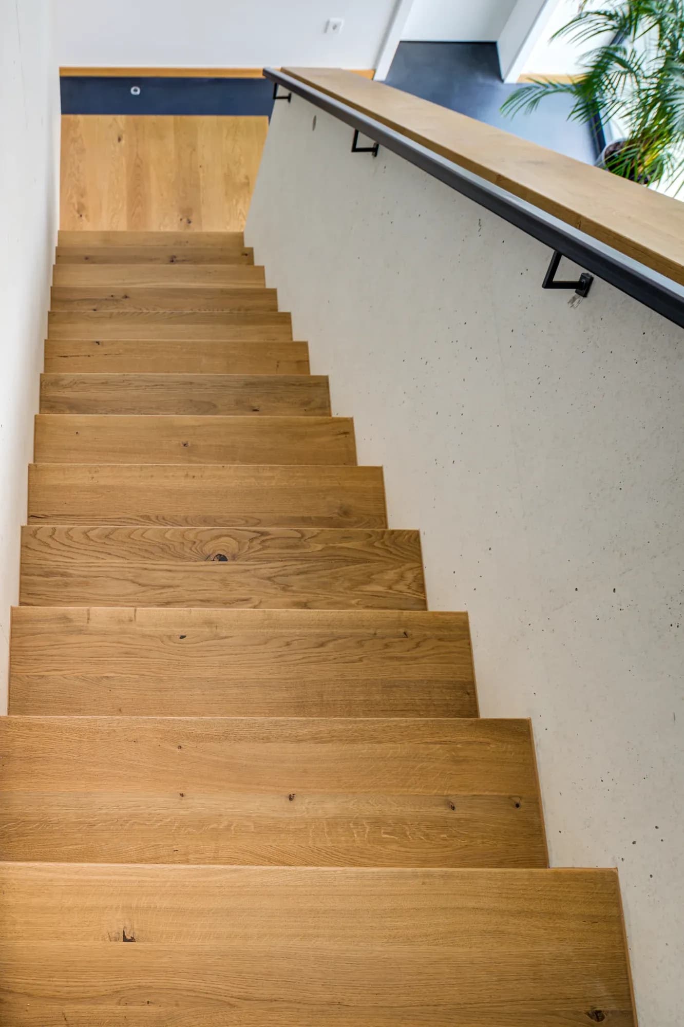Escalier en chêne massif à volée suspendue le long d'un mur blanc.