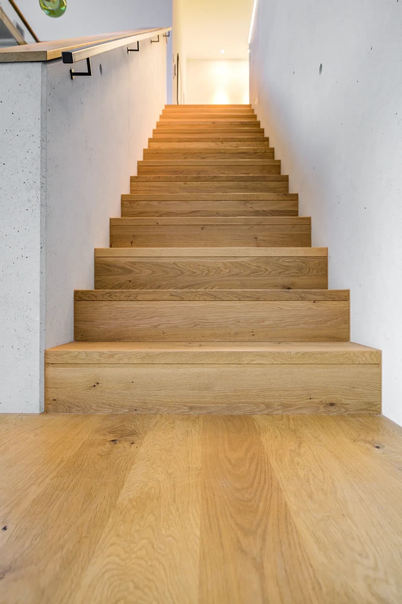 Vue d'un escalier en chêne menant vers l'étage éclairé.