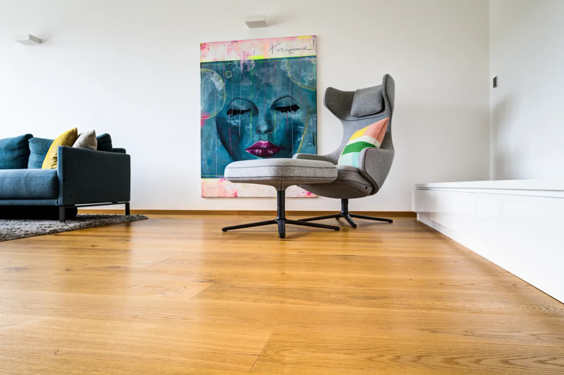 Séjour avec parquet en chêne style maison de campagne, canapé, fauteuil et œuvre d'art au mur.