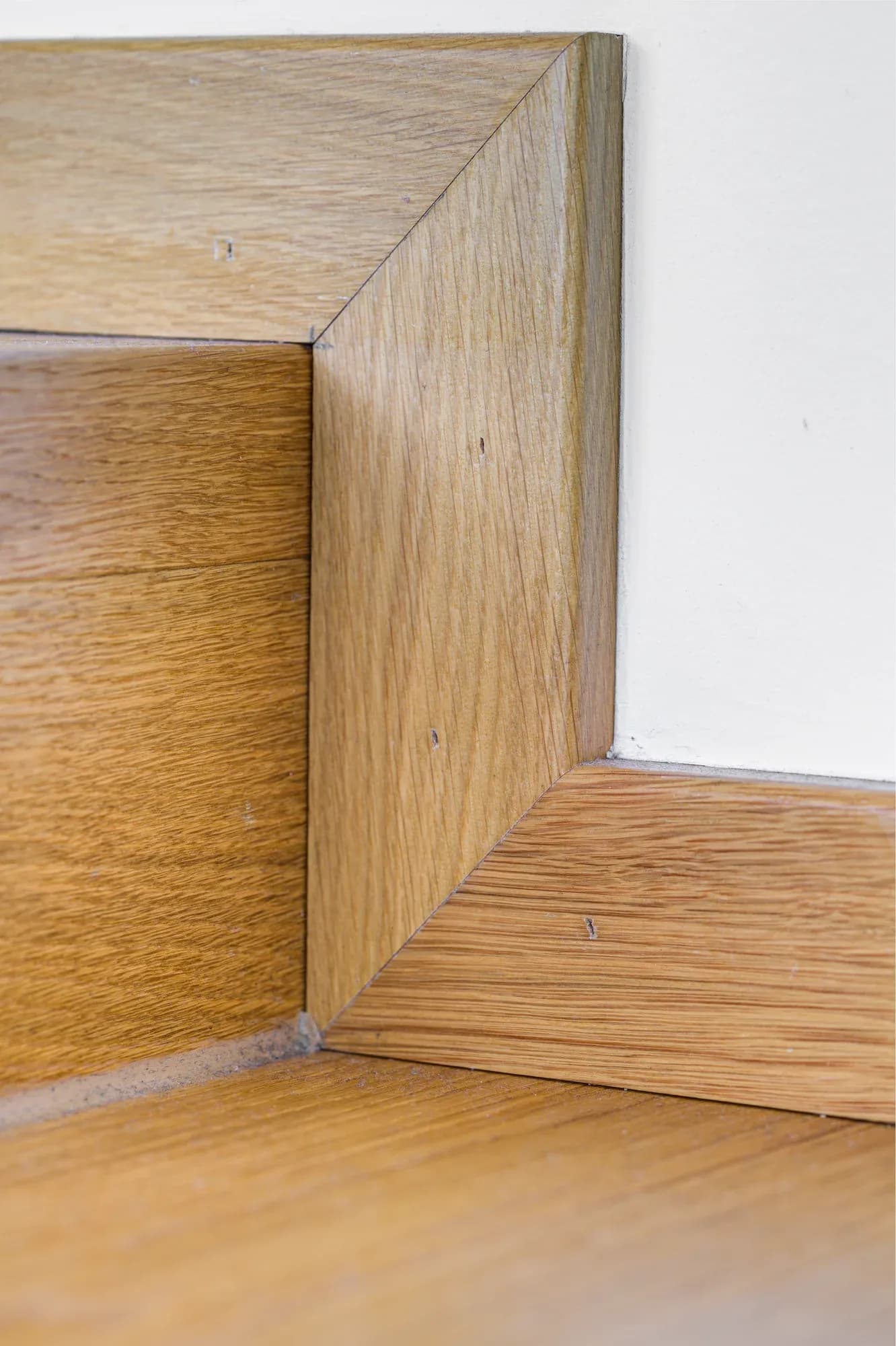 Habillage en chêne encastré à fleur sur une arête de mur, au-dessus du parquet.