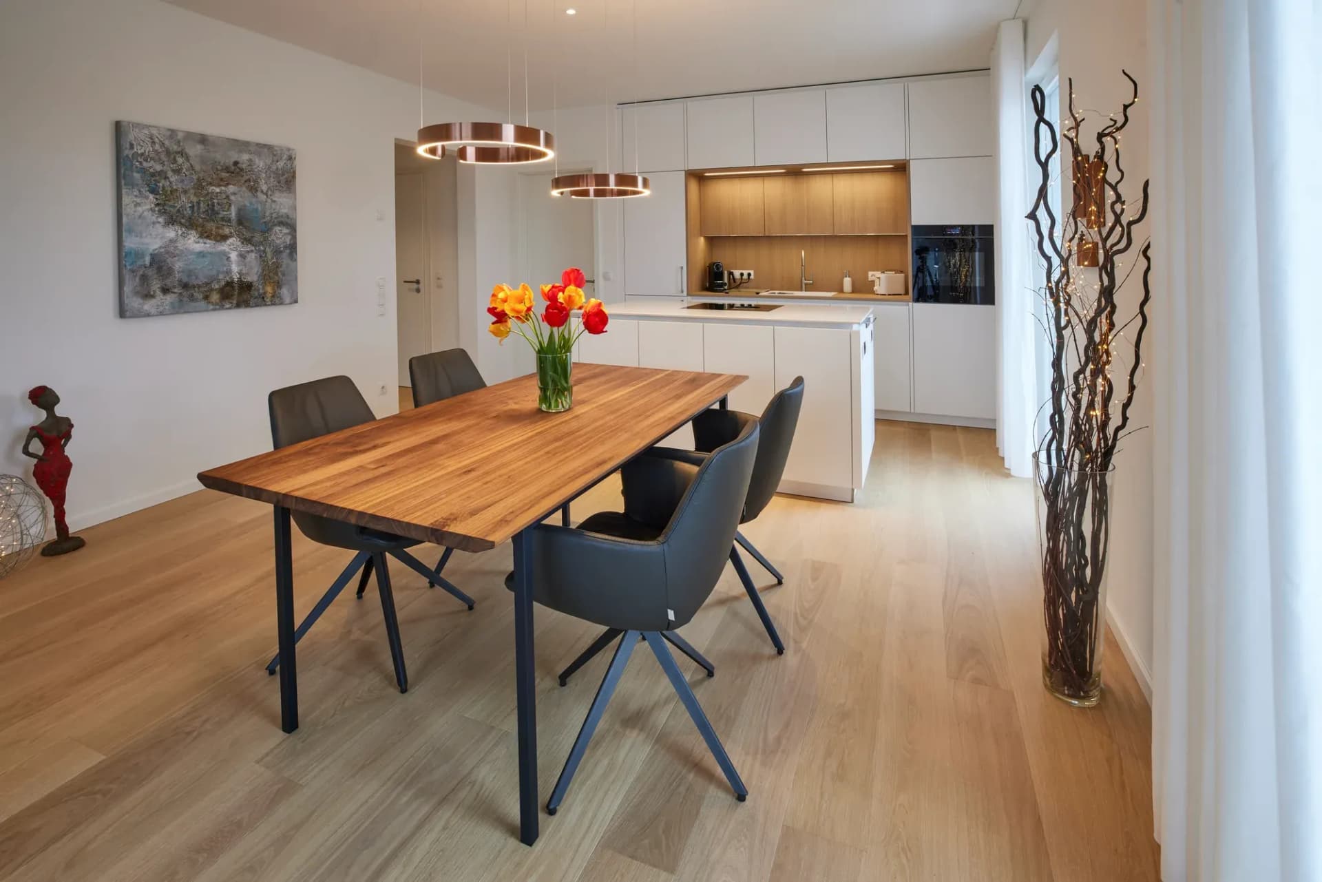 Espace de vie ouvert avec îlot de cuisine blanc cristal, table à manger en bois et parquet chêne style maison de campagne, suspension ronde au-dessus de la table.
