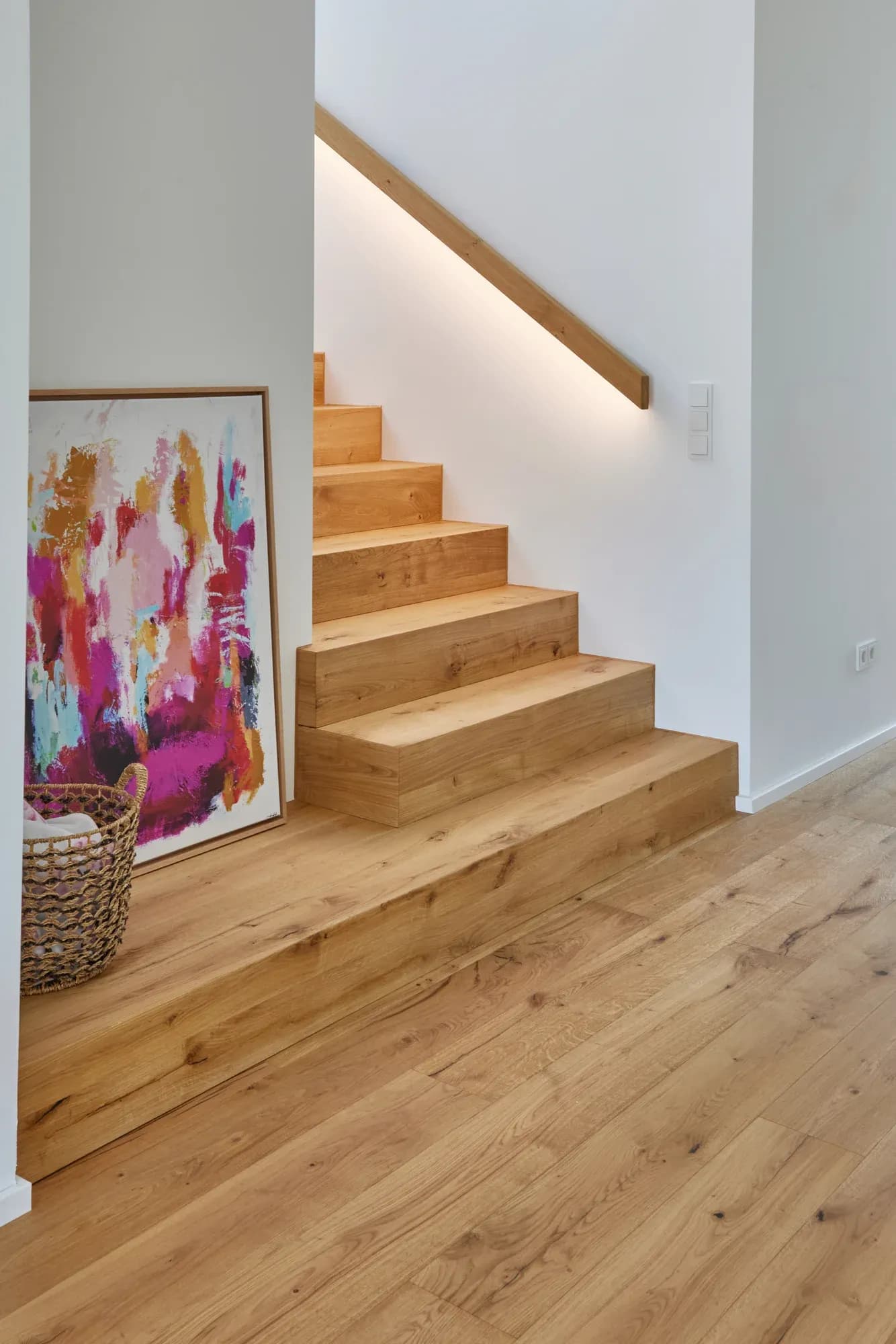 Escalier sculptural en chêne à structure pliée, s'élevant en courbe, accompagné d'une main courante en chêne encastrée dans le mur et éclairée par LED.